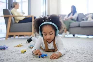 Fillette jouant par terre avec un casque sur les oreilles.